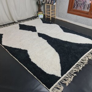 May include: Black and white geometric patterned rug with a fringe border. The rug has a modern design with a white background and black abstract shapes.