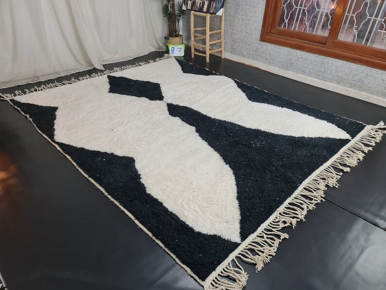 May include: Black and white geometric patterned rug with a fringe border. The rug has a modern design with a white background and black abstract shapes.