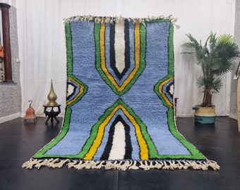 May include: A blue, green, yellow, white, and black Moroccan rug with a geometric pattern. The rug has fringe on the edges.