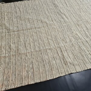Puede incluir: Una alfombra tejida blanca y marr&oacute;n con un patr&oacute;n a rayas. La alfombra est&aacute; hecha de un material suave y texturizado.