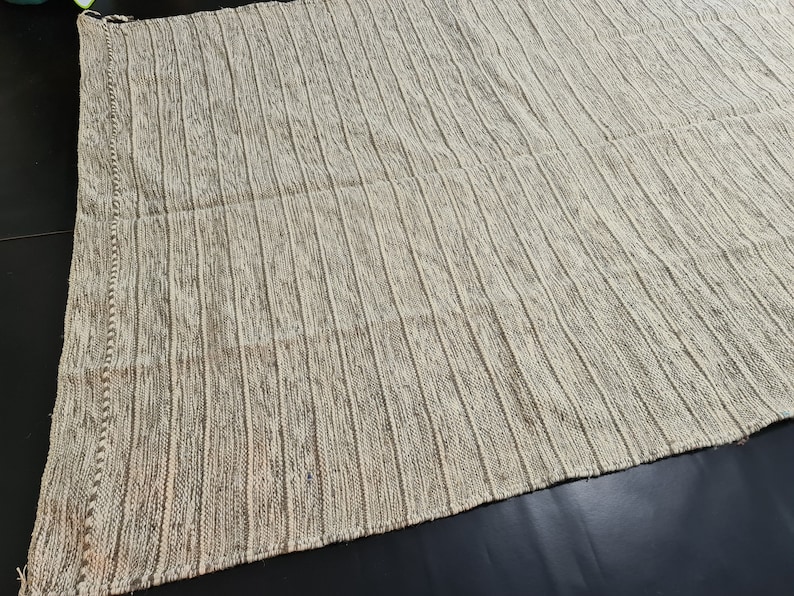 Puede incluir: Una alfombra tejida blanca y marr&oacute;n con un patr&oacute;n a rayas. La alfombra est&aacute; hecha de un material suave y texturizado.