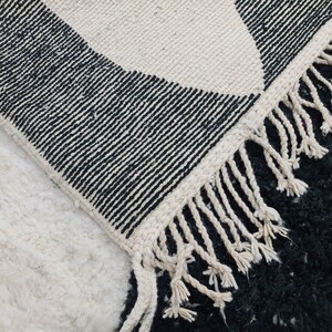 May include: Black and white patterned rug with a fringe border. The rug is made of wool and has a soft, textured feel.