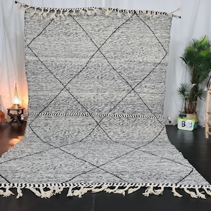 May include: A black and white Moroccan rug with a diamond pattern. The rug has a fringe border and is made of wool.