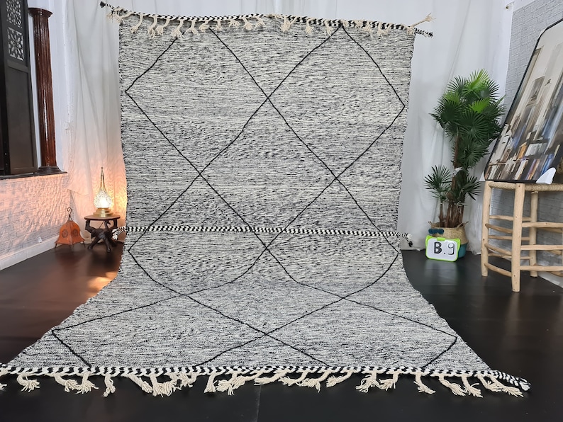 May include: A black and white Moroccan rug with a diamond pattern. The rug has a fringe border and is made of wool.