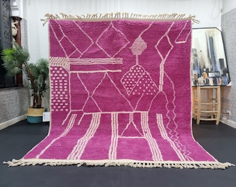 May include: A pink and white Moroccan rug with a geometric pattern. The rug has a fringe border and is made of wool.