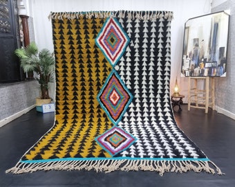 May include: A colorful Moroccan rug with a geometric pattern of black and white triangles and colorful diamonds. The rug has a fringe border.