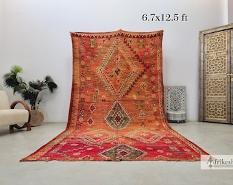 May include: A large, intricately patterned Moroccan rug in shades of red, orange, and green. The rug is 6.7 feet by 12.5 feet and features a diamond-shaped design.