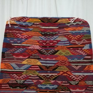 Pu&ograve; includere: Un tappeto colorato e fantasia con un design geometrico. Il tappeto presenta una variet&agrave; di colori, tra cui rosso, arancione, blu e giallo. Il design del tappeto &egrave; composto da forme e linee ripetute, creando un aspetto strutturato. Il tappeto &egrave; rettangolare e sembra essere fatto di tessuto tessuto.