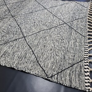 May include: Black and white area rug with a diamond pattern and fringe on the edges.