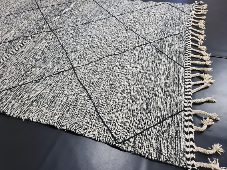 May include: Black and white area rug with a diamond pattern and fringe on the edges.