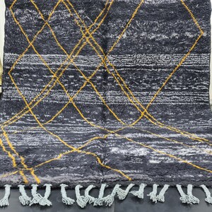 May include: A black and white rug with a geometric pattern of yellow lines. The rug has a fringe border.