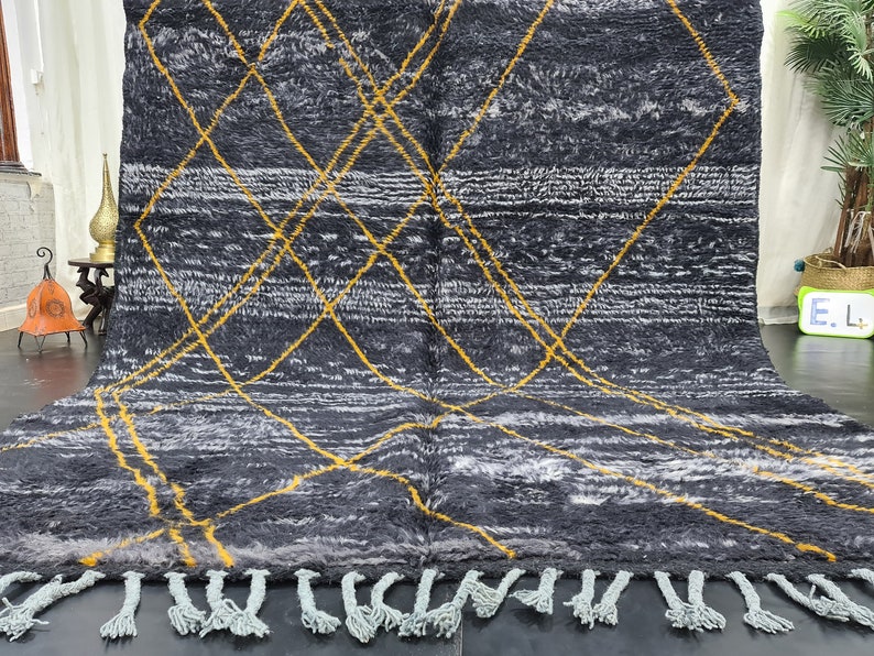 May include: A black and white rug with a geometric pattern of yellow lines. The rug has a fringe border.
