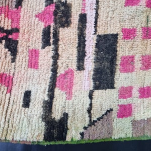 May include: A close-up of a colorful woven rug with pink, black, and white geometric patterns. The rug has a frayed edge and a textured surface.
