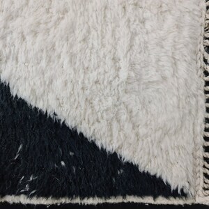 May include: A white and black rug with a geometric design. The rug has a fringe border.
