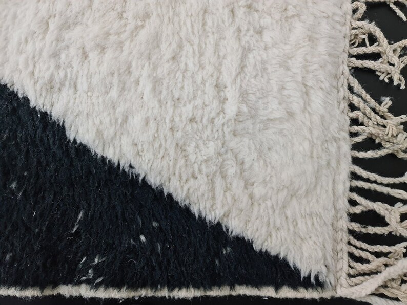 May include: A white and black rug with a geometric design. The rug has a fringe border.