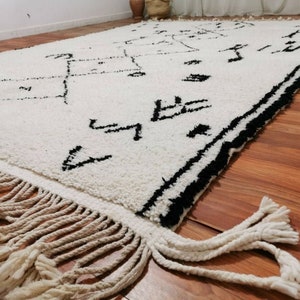 May include: A white and black Moroccan rug with a geometric pattern and fringe. The rug is made of wool and has a soft, plush texture.