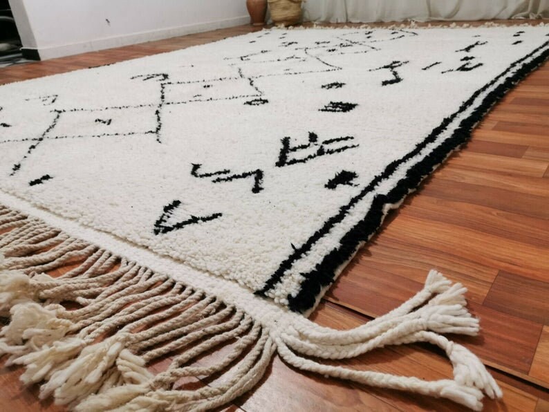 May include: A white and black Moroccan rug with a geometric pattern and fringe. The rug is made of wool and has a soft, plush texture.