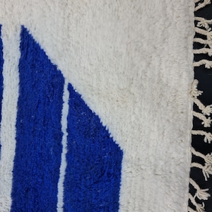 Puede incluir: Una alfombra blanca y azul con un patr&oacute;n geom&eacute;trico. La alfombra tiene un borde de flecos.