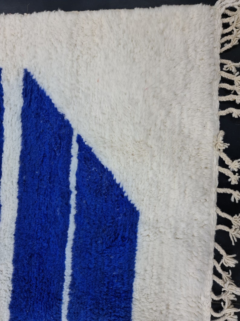 Puede incluir: Una alfombra blanca y azul con un patr&oacute;n geom&eacute;trico. La alfombra tiene un borde de flecos.