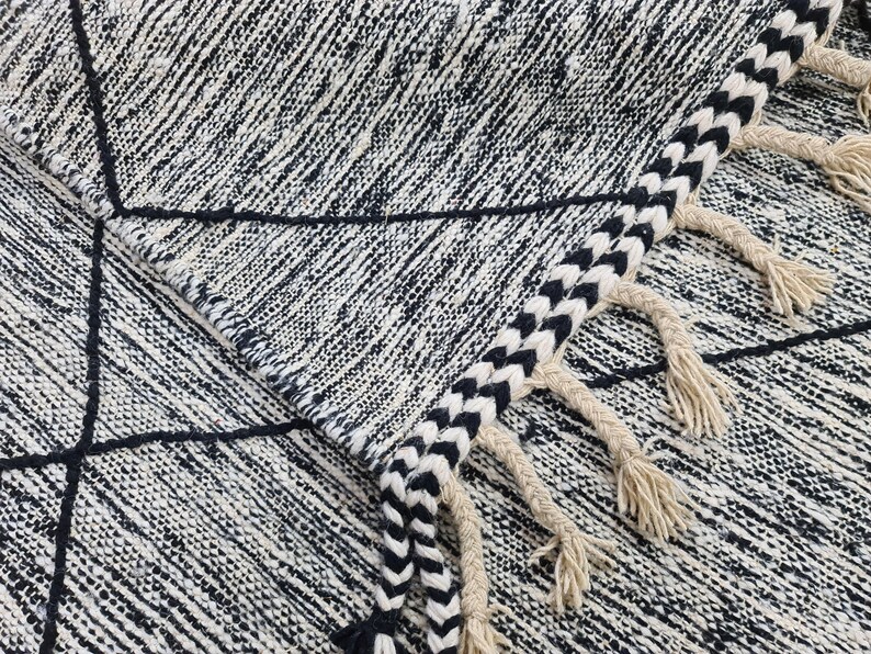 May include: Black and white geometric patterned rug with fringe. The rug has a woven texture and a black and white striped fringe.