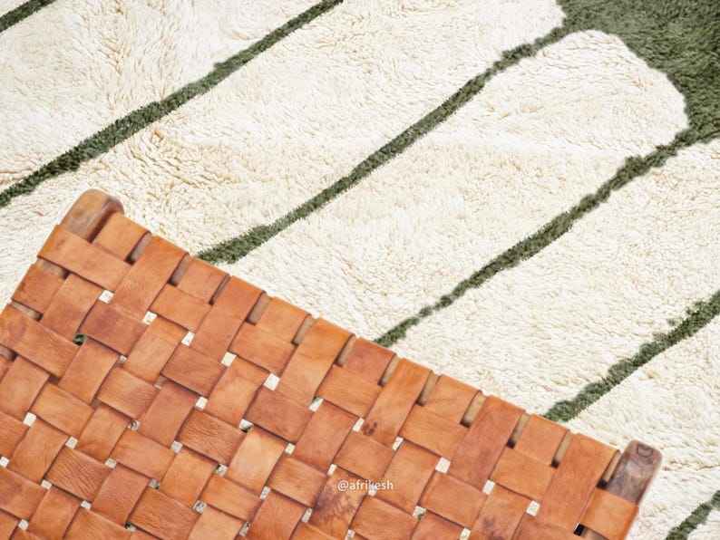 May include: A woven leather chair with a light brown hue is positioned diagonally, partially obscuring a textured rug. The rug features a cream-colored base with dark green stripes. The chair's design showcases a grid-like pattern.