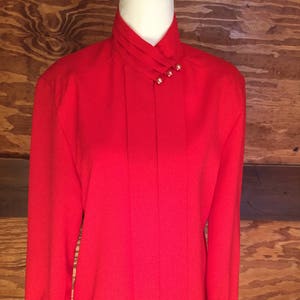 Puede incluir: Una blusa roja de manga larga con cuello alto y botones de perla.