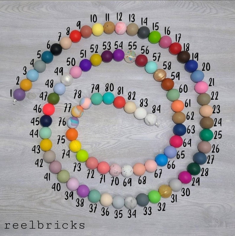 May include: A colorful set of 84 round beads, numbered 1 through 84, arranged in a circle. The beads are made of silicone and come in a variety of colors, including red, blue, green, yellow, pink, purple, orange, and brown.