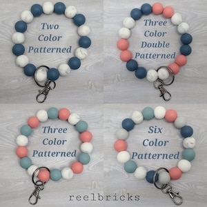 May include: Four silicone beaded keychains in different color combinations. The keychains are made with blue, white, gray, and pink beads. The beads have a marble pattern. The keychains are labeled with the number of colors used and the word "patterned".