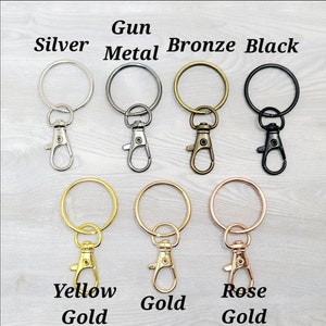 May include: Assortment of keychains in various metal finishes, including silver, gun metal, bronze, black, yellow gold, gold, and rose gold. Each keychain features a round ring and a lobster claw clasp.