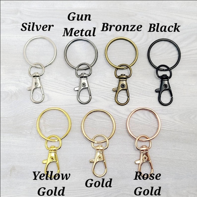 May include: Assortment of keychains in various metal finishes, including silver, gun metal, bronze, black, yellow gold, gold, and rose gold. Each keychain features a round ring and a lobster claw clasp.