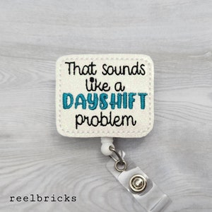 May include: White glitter badge holder with a blue and black embroidered saying "That sounds like a day shift problem".