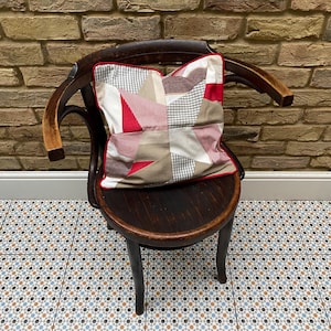 May include: A wooden chair with a patchwork cushion in shades of red, beige, and white. The chair is sitting on a patterned tile floor.
