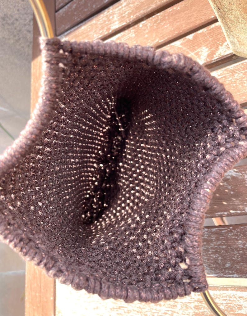Pu&ograve; includere: Una borsa all'uncinetto marrone scuro, a trama aperta, con un manico color oro. La trama della borsa &egrave; visibile, con un motivo di piccoli fori. Il manico ha un design semplice e curvo. La borsa &egrave; probabilmente fatta a mano.