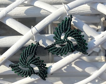 May include: A pair of dark green macrame earrings. Each earring has a triangular design with a spiral pattern and small green beads. The earrings hang from silver hooks, showcasing a handcrafted jewelry item.