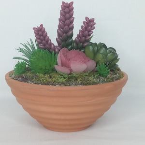 May include: A terracotta pot with a variety of artificial succulents, including pink and green varieties. The pot has a wavy, textured surface.