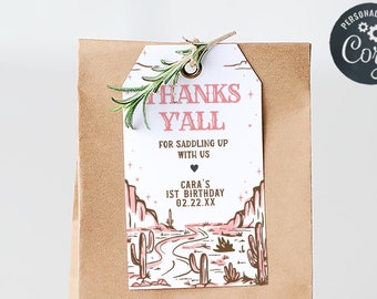 Könnte beinhalten: Eine braune Papiertüte mit einem weißen Etikett. Das Etikett zeigt eine rosa und braune Illustration einer Wüstenlandschaft mit Kakteen und einer Straße. Der Text auf dem Etikett lautet "Thanks Y'all" und "Cara's 1st Birthday 02.22.XX".