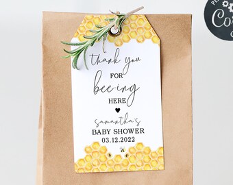 May include: A brown paper bag with a yellow and white gift tag that says "Thank you for bee-ing here, Samantha's Baby Shower 03.12.2022".