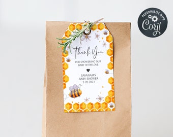 May include: A brown paper bag with a thank you tag attached. The tag is decorated with a bee and honeycomb pattern and says "Thank You for showering our baby with love, Savannah's Baby Shower 5.20.2023".