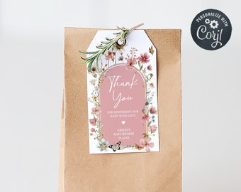 May include: A brown paper bag with a floral thank you tag attached. The tag has a pink background with a floral border and the text "Thank You" for showering our baby with love.  Ashley's Baby Shower 01.28.23.
