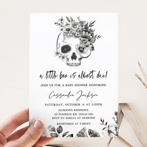K&ouml;nnte beinhalten: Eine Babyparty-Einladung mit einem Totenkopf-Design, verziert mit floralen Elementen. Der Text lautet "a little boo is almost due!" und enth&auml;lt Veranstaltungsdetails wie Datum, Uhrzeit und Ort.