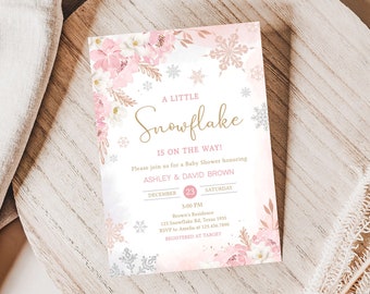 Könnte beinhalten: Eine Babyparty-Einladung mit Aquarelldesign. Die Einladung zeigt den Text "A Little Snowflake Is On The Way!" in goldener Schrift. Rosa und weiße Blumen- und Schneeflocken-Akzente umrahmen den Text. Das Datum ist der 23. Dezember.