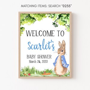 May include: A baby shower welcome sign with a watercolor illustration of Peter Rabbit wearing a blue jacket. The sign says "Welcome to Scarlet's Baby Shower March 26, 2023".
