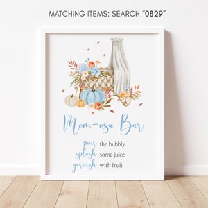 May include: A framed print with a watercolor design. The artwork features a baby cradle, pumpkins, and floral arrangements in shades of blue, orange, and white. The text "Mom-osa Bar" is displayed in a script font, along with instructions.