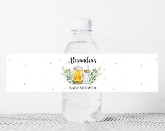 May include: Water bottle label with a gold and green design. The label says "Alexandra's Baby Shower" and features a beer mug and a baby bottle.