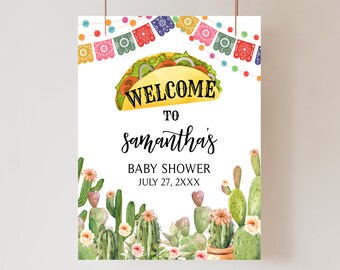 May include: A welcome sign for a baby shower with a colorful taco graphic and the text "Welcome to Samantha's Baby Shower July 27, 2XXX". The sign is decorated with a string of colorful paper flags and green cactus plants.