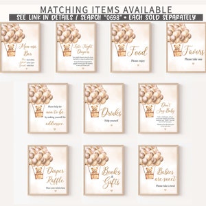 May include: Ten printable signs with a teddy bear in a hot air balloon design. The signs are for a baby shower and include titles like "Mon esa Bar", "Late Night Diapers", "Food", "Favors", "Drinks", "Don't Say Baby", "Diaper Raffle", "Books & Gifts", and "Babies are Sweet".
