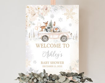 May include: A baby shower welcome sign featuring a vintage pink truck carrying woodland animals and balloons in a winter scene. The sign reads "Welcome to Ashley's Baby Shower December 23, 2XXX". The sign is displayed on a wooden easel.