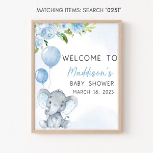 May include: A blue and gray baby shower welcome sign with a cute elephant holding blue balloons. The sign says "Welcome to Maddison's Baby Shower March 18, 2023".