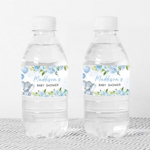 Op de afbeelding: Twee doorzichtige plastic waterflessen met blauwe en witte etiketten. De etiketten tonen een aquarel-illustratie van een babyolifant met blauwe ballonnen en bloemen. De tekst op de etiketten luidt "Maddison's Baby Shower".