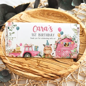 May include: A pink and white chocolate bar wrapper with a watercolor illustration of a farm scene. The wrapper says "Cara's 1st Birthday" and "Thank you for celebrating with us!"